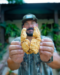 A man holding up freshly fried Cajun-style frog legs