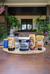 A lineup of ingredients set upon a table to make fried oyster poboys, including a quart of fresh oysters, spice containers, and sauce containers.