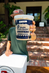 A person holding up a container of fresh Louisiana oysters being used to make fried oyster poboys.