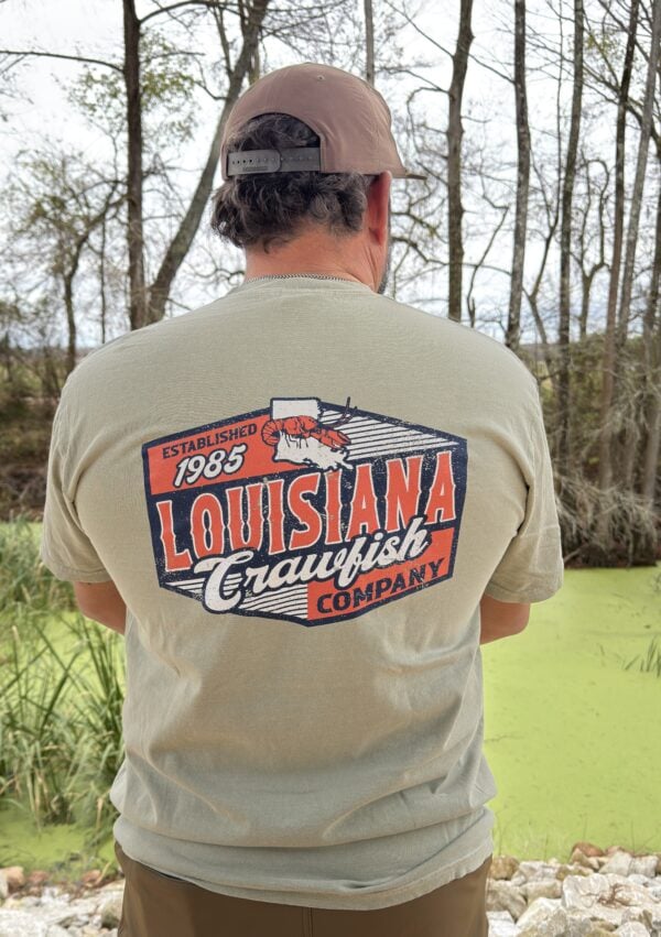 2026 back Outdoors, a person wears a “Louisiana Crawfish Company Established 1985” shirt, perfect for Boiled IQF Crawfish Party Packs.