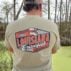 Outdoors, a person wears a “Louisiana Crawfish Company Established 1985” shirt, perfect for Boiled IQF Crawfish Party Packs.