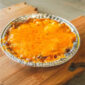 An 8oz serving of Rachael’s Crawfish Au Gratin, baked in a foil pan and served on a wooden board.