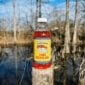 An 8oz bottle of LA Crawfish Co. Liquid Boil rests on a wooden post before a bayou.