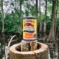A yellow canister of LA Crawfish Co. Creole Seasoning stands on a tree stump before a bayou.