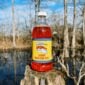 A 16oz bottle of LA Crawfish Co. Liquid Boil resting on a tree stump by a swamp.