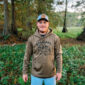 A man outdoors wearing a baseball cap and a light brown LA Crawfish Co. Sport-Tek hoodie with a crawfish graphic.