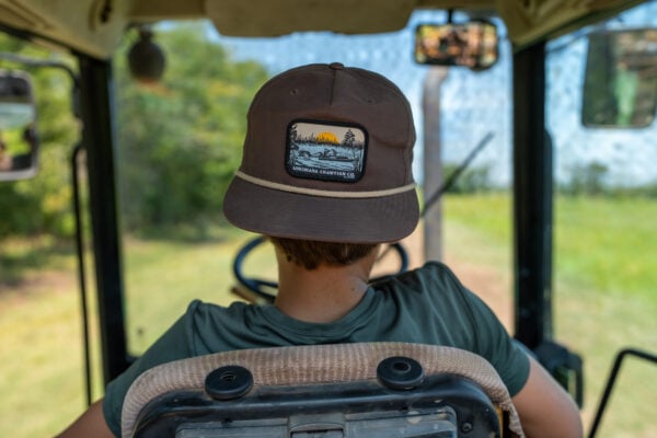 boat patch grandpa (branch) View from inside a tractor cabin, showing a person wearing a brown LA Crawfish Co. Boat Patch Grandpa hat.