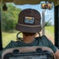 View from inside a tractor cabin, showing a person wearing a brown LA Crawfish Co. Boat Patch Grandpa hat.