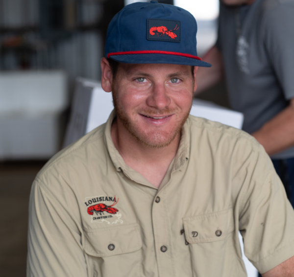 A man wears a blue LA Crawfish Co. PVC patch hat and a matching button-down shirt featuring a crawfish logo.