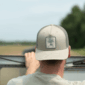 Back view of a person wearing a beige mesh-back Swamp Bottom Patch Hat with a rectangular tree illustration.