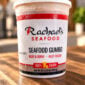 A frosted Rachael’s Sampler container of seafood gumbo sitting on a wooden surface.