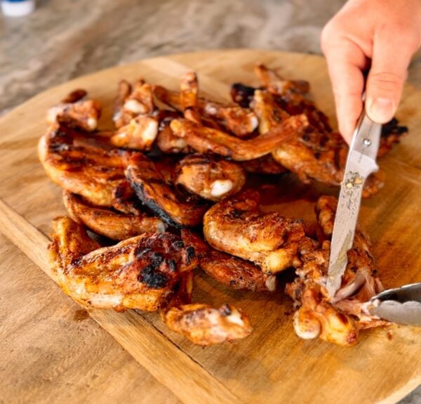 Alligator Legs - Bone In 2lb (Marinated) -2 A hand uses a knife to cut cooked, bone-in alligator legs on a wooden cutting board.