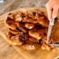 A hand uses a knife to cut cooked, bone-in alligator legs on a wooden cutting board.