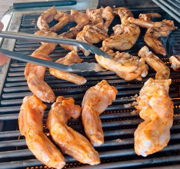 Alligator Legs - Bone In 2lb (Marintated) -1 Metal tongs turning 5 lb of seasoned, bone-in alligator legs on a grill.