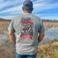 A man in a cap stands by a wet field, wearing a gray 2025 LA Crawfish Co. 40th Anniversary shirt celebrating Louisiana seafood.