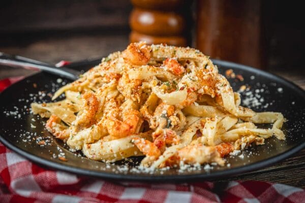 Crawfish fettuccine with Louisiana flavors served on a black plate, set on a red and white checkered cloth.