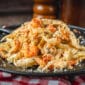 Crawfish fettuccine with Louisiana flavors served on a black plate, set on a red and white checkered cloth.
