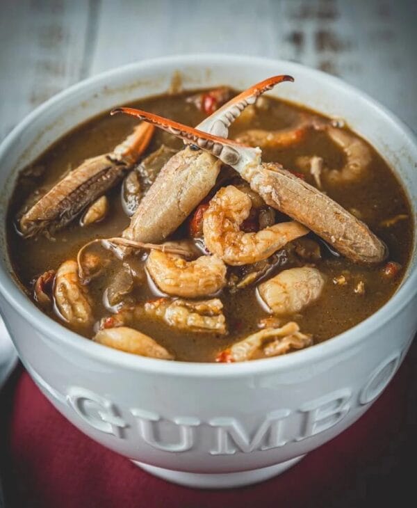 Seafood gumbo with shrimp and crab in rich broth, served in a white bowl on a red napkin.