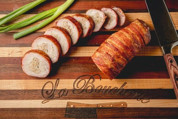 Sliced stuffed pork tenderloin with boudin on a board, green onions, knife, and “La Boucherie” engraving—perfect for Cajun fans.