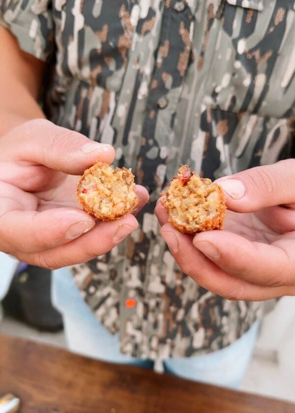 boulettes open Hands break open a fried, breaded shrimp and crab boulette, showing a chunky seafood filling inside.