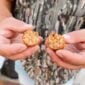 Hands break open a fried, breaded shrimp and crab boulette, showing a chunky seafood filling inside.