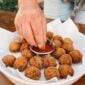 A hand dips a Shrimp and Crab Boulette into red sauce, served alongside a platter of fried appetizers.