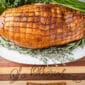 A cooked 5 lb La Boucherie Turducken Roll sits on a white platter garnished with herbs atop a wooden table.