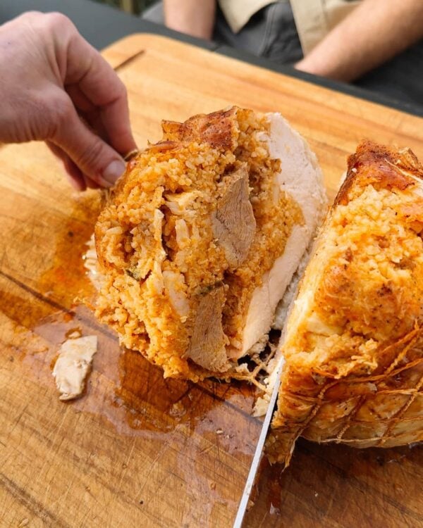 turducken roll sliced A hand holds a sliced 5 lb LA Crawfish Co. Turducken Roll with stuffing on a wooden cutting board.