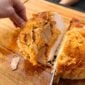 A hand holds a sliced 5 lb LA Crawfish Co. Turducken Roll with stuffing on a wooden cutting board.