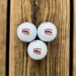 Three white LA Crawfish Co. golf balls with Louisiana logos rest on a wooden surface, ideal for Louisiana fans.