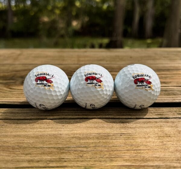 LA-Crawfish-Co.-Golf-Balls-3-edited__22259.1758819496.1280.1280.jpg Three LA Crawfish Co. golf balls with LSU logos, lined up on wood, capture a touch of Cajun flair.