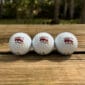 Three LA Crawfish Co. golf balls with LSU logos, lined up on wood, capture a touch of Cajun flair.