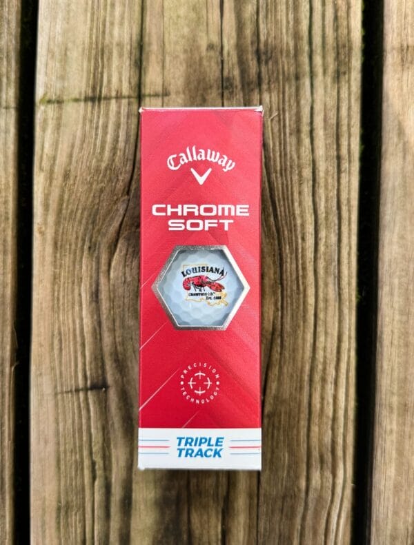 LA-Crawfish-Co.-Golf-Balls-edited__31535.1758819121.1280.1280.jpg A box of LA Crawfish Co. golf balls featuring a crawfish logo sits on a wooden surface.