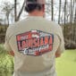 Near a pond, a person wearing a 2026 LA Crawfish Co T-shirt enjoys authentic Louisiana crawfish tradition.
