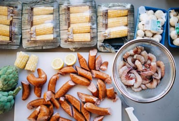 Sliced sausage, shrimp, corn, mushrooms, and artichoke suggest a classic Cajun seafood feast from Louisiana.