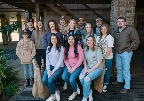 Thirteen people, some standing and some sitting, gather outside a wooden building, ready to enjoy Louisiana seafood together.
