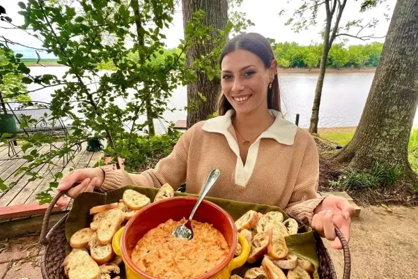 Outdoors by trees and water, a woman serves Louisiana seafood dip with toasted bread—ideal for Cajun food fans.
