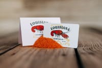 Two Louisiana Crawfish Co. cards behind a heap of orange cajun seasoning on a rustic wooden table.