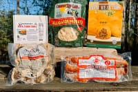 Five packaged foods—Cajun meats, sausage, and cheese—are arranged on a wooden surface outdoors.