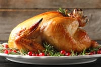 A whole roasted turkey sits on a white platter with rosemary, cranberries, and Cajun meats, set on a wooden background.