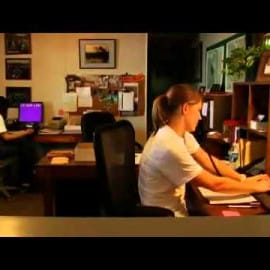 Two people sit at desks with computers in an office, talking on the phone about Louisiana seafood and Cajun cuisine.