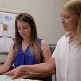 Two women study a large map indoors, planning to order Louisiana seafood and Cajun foods like crawfish for nationwide shipping.