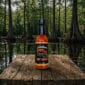 Louisiana Crawfish Co. Hot Sauce on a table beside a swamp, perfect for adding heat to Cajun food and seafood dishes.